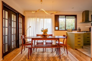 Un comedor con una mesa y sillas de madera, un florero con flores, y una ventana con cortinas.