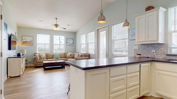A spacious living room with a sofa, a coffee table, and a kitchen area with white cabinets and a large island. - Candy's Cove: 2  BR, 1  BA House in Crystal Beach, Sleeps 8 (Crystal Beach)