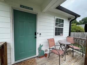 A green door with a sign above it, a small table with two chairs, and a wooden deck.