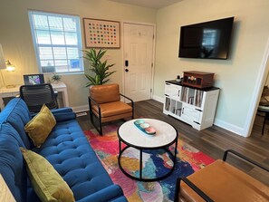 A living room with a blue sofa, a brown chair, a round coffee table, a TV, and a cabinet with books.