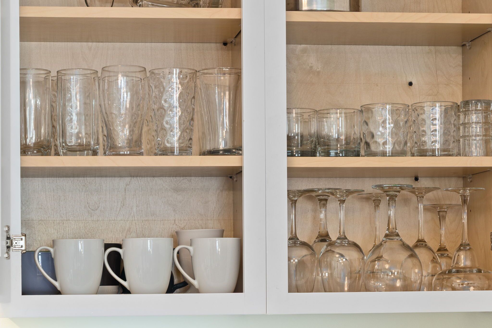 Un meuble avec des étagères contenant divers articles en verre, notamment des verres à boire et des verres à vin.
