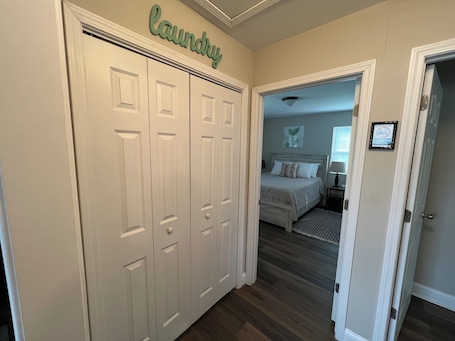 A hallway leading to a bedroom with a bed, a nightstand, and a wall-mounted artwork.. Quiet 2BR Cottage - 3.9 miles to downtown Durham + close to Duke, DPAC and NCCU