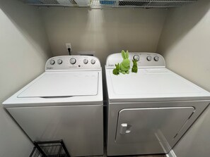 Two white Whirlpool washers in a laundry room with a metal shelf above.