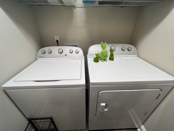 Dos lavadoras Whirlpool blancas en un cuarto de lavado con un estante de metal arriba.
