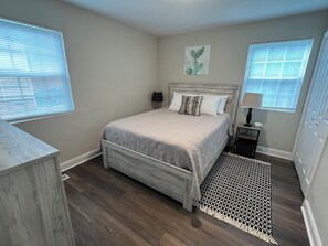 A bedroom with a bed, bedside tables, a lamp, a wall art piece, and a patterned rug. - Quiet 2BR Cottage - 3.9 miles to downtown Durham + close to Duke, DPAC and NCCU (Durham)