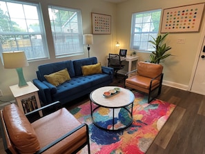 A living room with a blue sofa, a round coffee table, a brown leather chair, and a colorful rug.