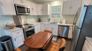 Una cocina moderna con armarios blancos, electrodomésticos de acero inoxidable, una mesa de comedor de madera y dos sillas.