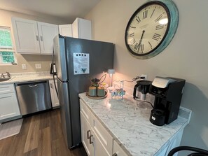 A modern kitchen with a stainless steel refrigerator, a clock on the wall, a coffee maker, and a small plant on the counter.