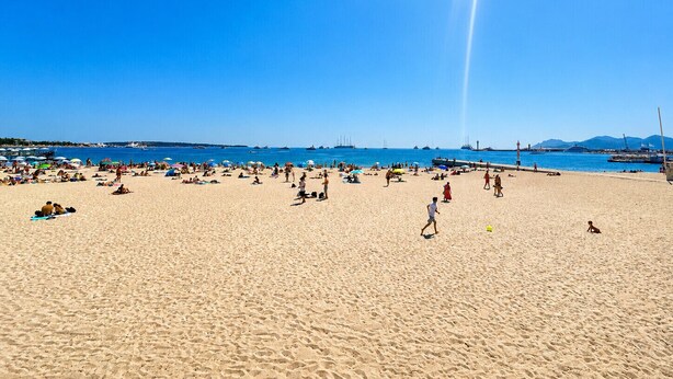 A beach with people sunbathing and walking, a clear sky, and boats in the water. - MIMOSAS 1 Air-conditioned near Croisette (Cannes)