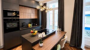 A modern kitchen with dark cabinetry, a central island, and a dining area with a wooden table and chairs. - MIMOSAS 1 Air-conditioned near Croisette (Cannes)