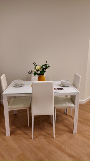 A dining table with two white chairs, a yellow vase with flowers, and a white tablecloth.