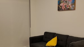 A living room with a grey sectional sofa, a yellow pillow, a painting of flowers, and a sliding door. - The Central Luxe (Surrey)