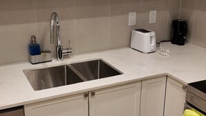 A kitchen with white cabinets, a stainless steel sink, a toaster, and a coffee maker. - The Central Luxe (Surrey)