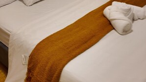 A neatly made bed with white bedding and a brown throw blanket, a white pillow, and a folded white towel on the bed. - The Central Luxe (Surrey)