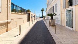 Une rue étroite en milieu urbain, bordée de bâtiments des deux côtés, avec un ciel dégagé et un trottoir pour les piétons.
