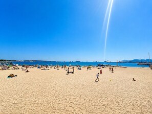 A beach with people sunbathing and walking, a clear sky, and boats in the water. - GIGI Urban Chic Centre Cannes Croisette on foot (Cannes)