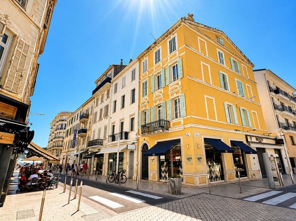 A multi-story building with a yellow facade, storefronts on the ground floor, and a pedestrian area with outdoor seating. - GIGI Urban Chic Centre Cannes Croisette on foot (Cannes)