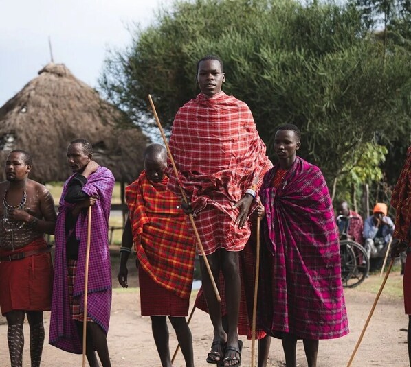 Un grupo de personas vestidas con atuendo tradicional, de pie al aire libre con una estructura de paja al fondo.