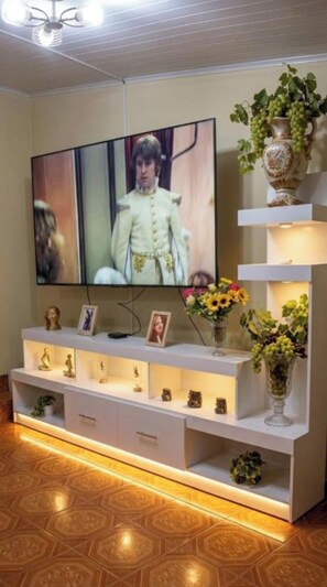 A living room with a flat-screen TV, a white entertainment unit with shelves, and a vase with flowers. - Apartamento carlos Goussen  (Granada)