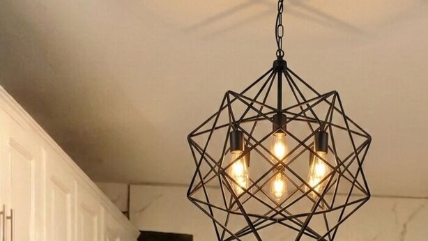 Una cucina moderna con mobili bianchi, una lampada a sospensione geometrica e un vaso con fiori rosa sul piano di lavoro.