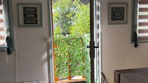 Quarto com um banco de madeira, uma mesa de jantar e uma porta que dá para um jardim com vista para árvores e uma cerca.