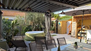 Um pátio externo com mesa de vidro, cadeiras, hidromassagem e uma estrutura de madeira com uma placa.