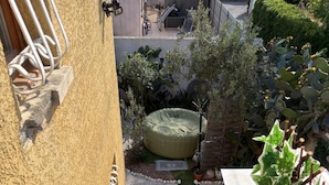 Escadaria de madeira que leva a um jardim no terraço, com área de estar circular e verde, um vaso de planta e corrimão de metal.