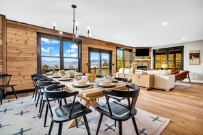 Un espace repas moderne avec une longue table en bois, des chaises noires et un lustre.