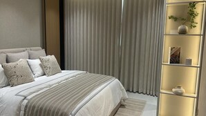 Un dormitorio con cama, cortinas, una estantería con objetos decorativos y una ventana.