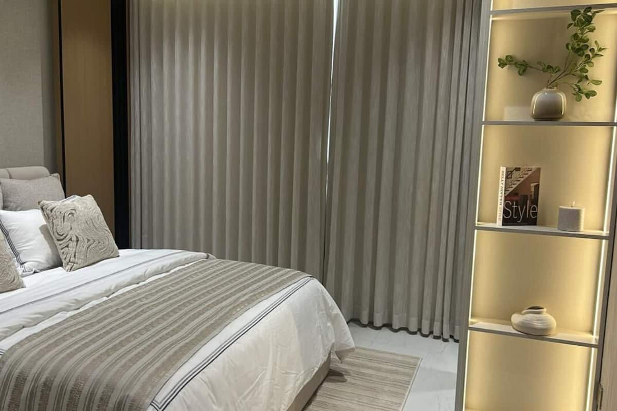 Un dormitorio con cama, cortinas, una estantería con objetos decorativos y una ventana.