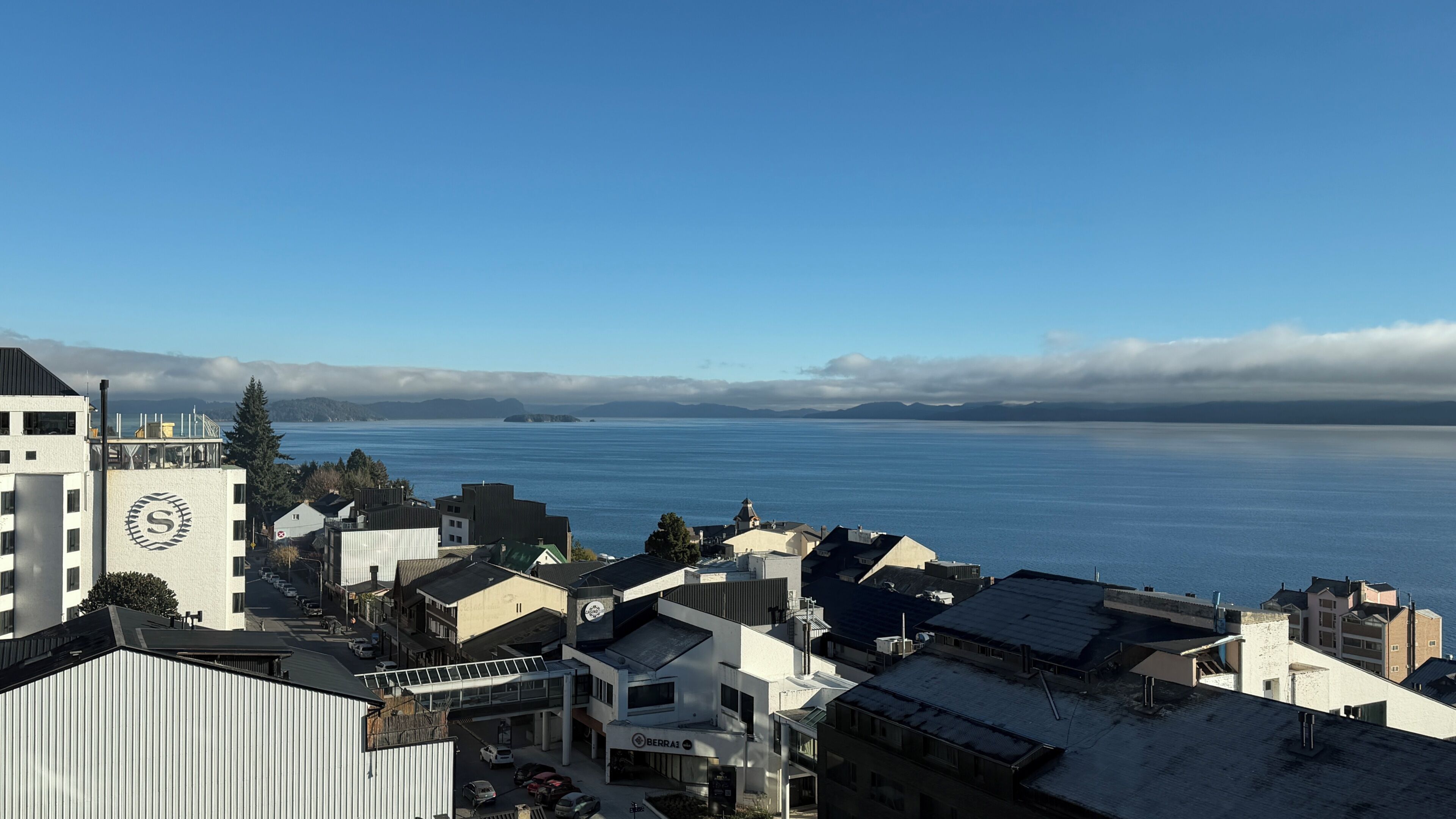 A coastal cityscape with buildings, a clear sky, and a view of the sea.