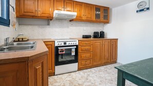 Una cocina con armarios de madera, estufa, pileta y un reloj en la pared.