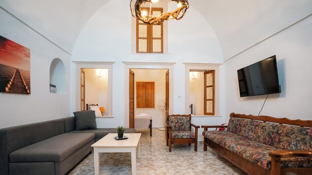 Una sala de estar con sofá, una silla, una mesa, un televisor y una puerta que da a otra habitación.