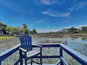 A wooden chair on a deck overlooking a marshy area with a clear blue sky. - Serenity View | Fenced Yard, Private Dock, Pet-Friendly (Tybee Island)