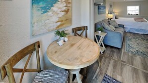 Una sala de estar con una mesa redonda de madera, dos sillas de madera, un sofá y un cuadro de una playa en la pared.