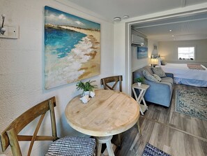 A living room with a round wooden table, two wooden chairs, a sofa, and a painting of a beach scene on the wall. - Serenity View | Fenced Yard, Private Dock, Pet-Friendly (Tybee Island)