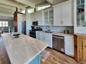 A modern kitchen with white cabinetry, a marble countertop, and a built-in dishwasher. - Serenity View | Fenced Yard, Private Dock, Pet-Friendly (Tybee Island)