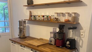 Cozinha com armários brancos, bancada de madeira, cafeteira, liquidificador e lixeira.