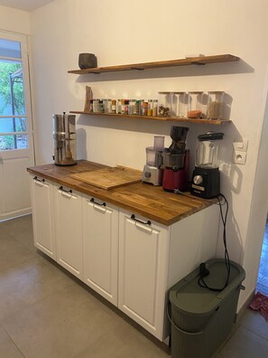 A kitchen with white cabinets, a wooden countertop, a coffee maker, a blender, and a trash bin. - Charming house in Toulon (Toulon)