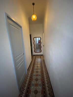 A hallway with a patterned floor, a door on the left, and a hanging light fixture. - Charming house in Toulon (Toulon)