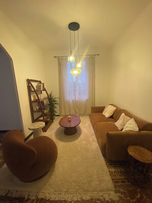 A living room with a brown sofa, a round coffee table, a wooden side table, a bookshelf, and a hanging light fixture. - Charming house in Toulon (Toulon)