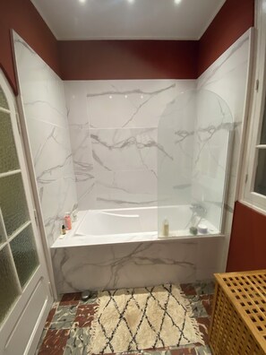 A bathroom with a marble wall, a bathtub, a shower, and a patterned rug. - Charming house in Toulon (Toulon)