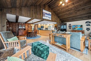 A spacious living area with wooden walls, a dining set, and a kitchen in the background.