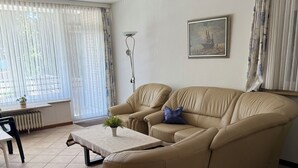 Un salon avec un canapé beige, une petite table, un lampadaire et un tableau accroché au mur.