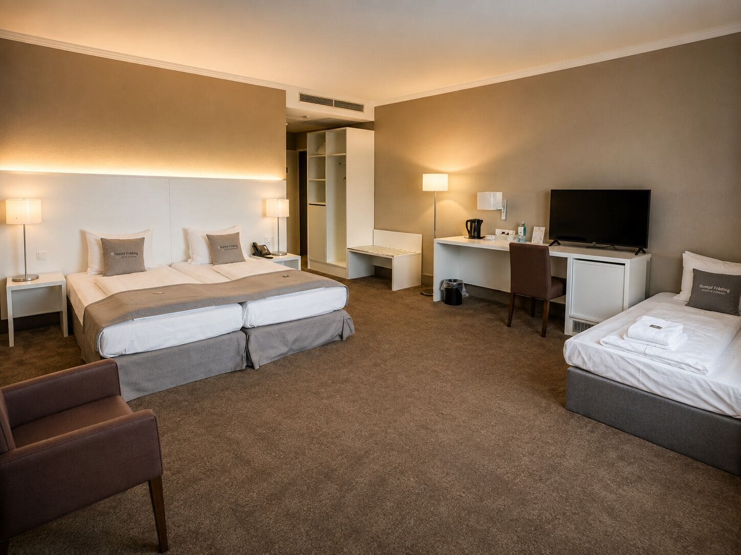 A hotel room with a bed, desk, chair, TV, and a walk-in closet.