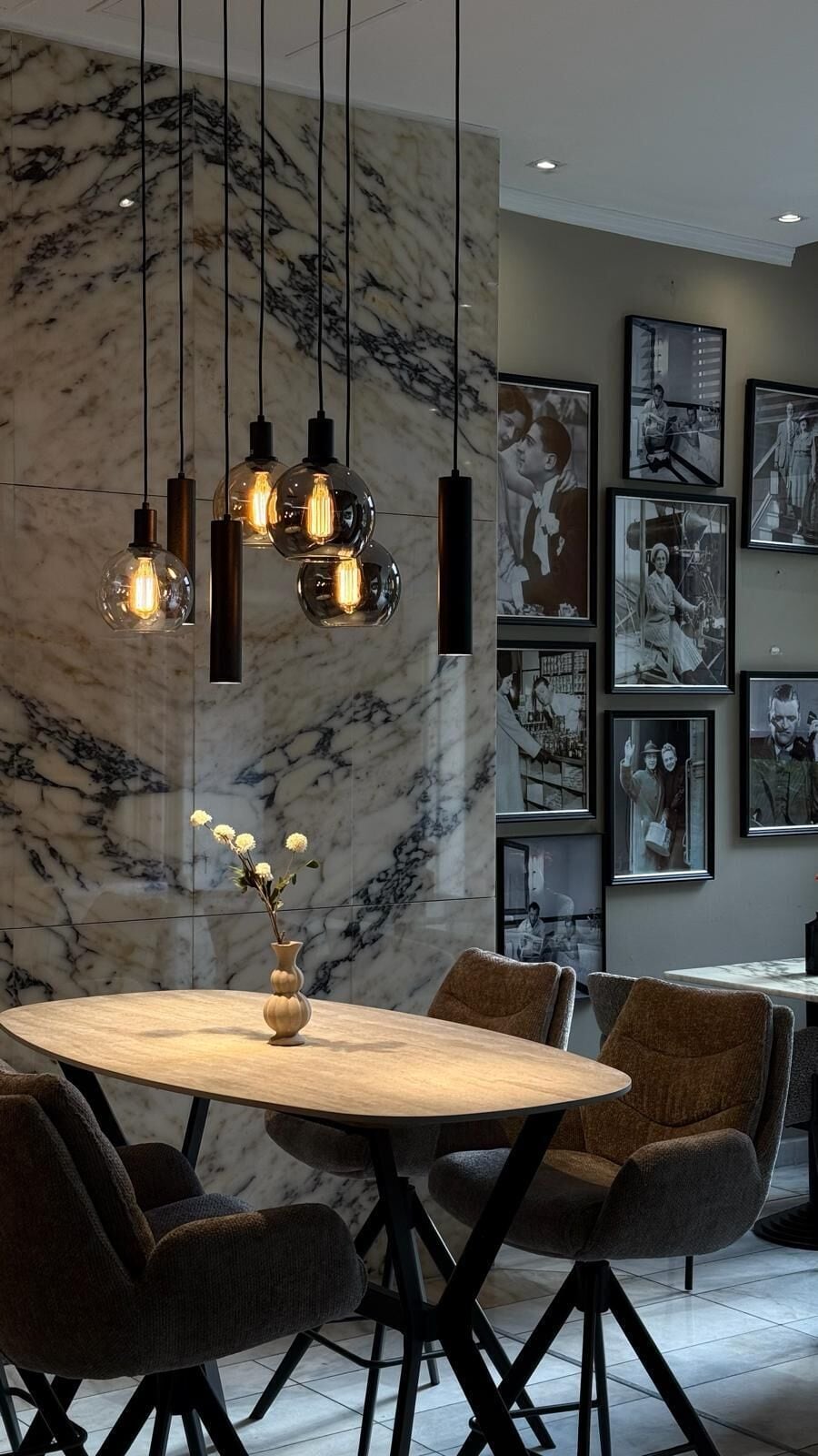 Un espace de salle à manger moderne avec un mur en marbre, des suspensions lumineuses, une table ronde en bois et des chaises rembourrées.