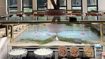 Um restaurante com uma grande árvore de cerejeira artificial, uma vitrine de vidro com diversos itens alimentícios e uma área de estar com mesas e cadeiras.