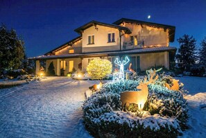 Ein zweistöckiges Haus mit einem verschneiten Einfahrt und beleuchteten Gartendekorationen.