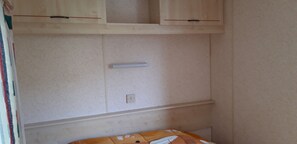 A room with a bed, a light switch, and a wall with a shelf above.