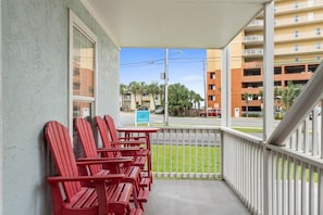 A balcony with red Adirondack chairs and a view of a parking lot and buildings. - Sleeps 4 2 Bedroom Beach Access Across Street Pool (PANAMA CITY BEACH)
